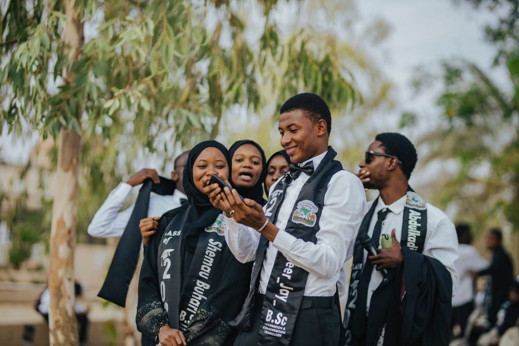 Jeunes diplômés regardant un téléphone ensemble après la remise des diplômes